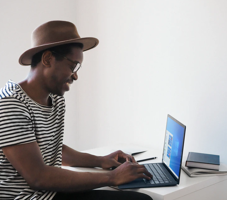 manitoba's online academic services , male wearing hat and glasses smiling, staring at laptop screen