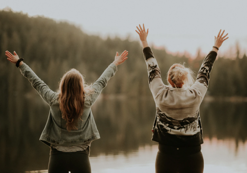 activities for mcmaster students , two women standing in front of a lake, backs to the camera and arms raised in the air