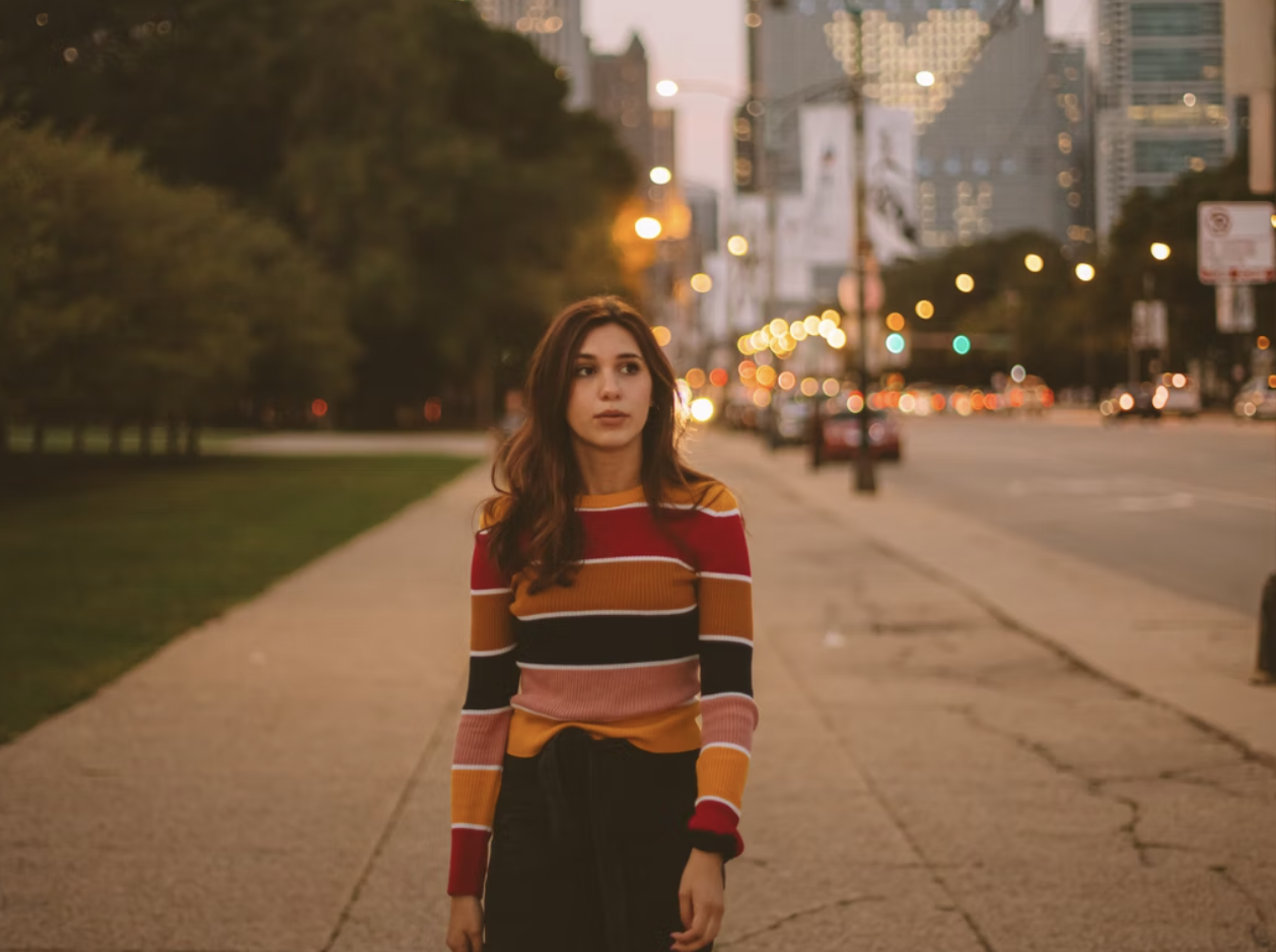 girl with brown hair and striped sweater walking down street