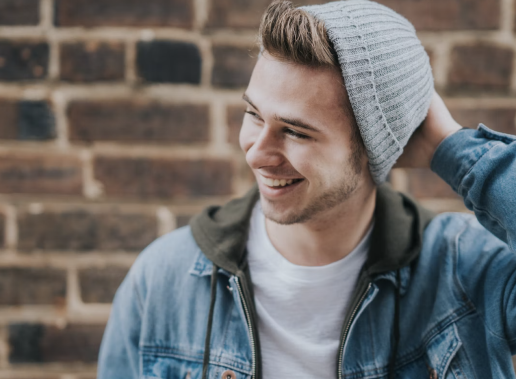 guy holding back of grey knit hat wearing jean jacket, smiling away from the camera, montreal's top student services