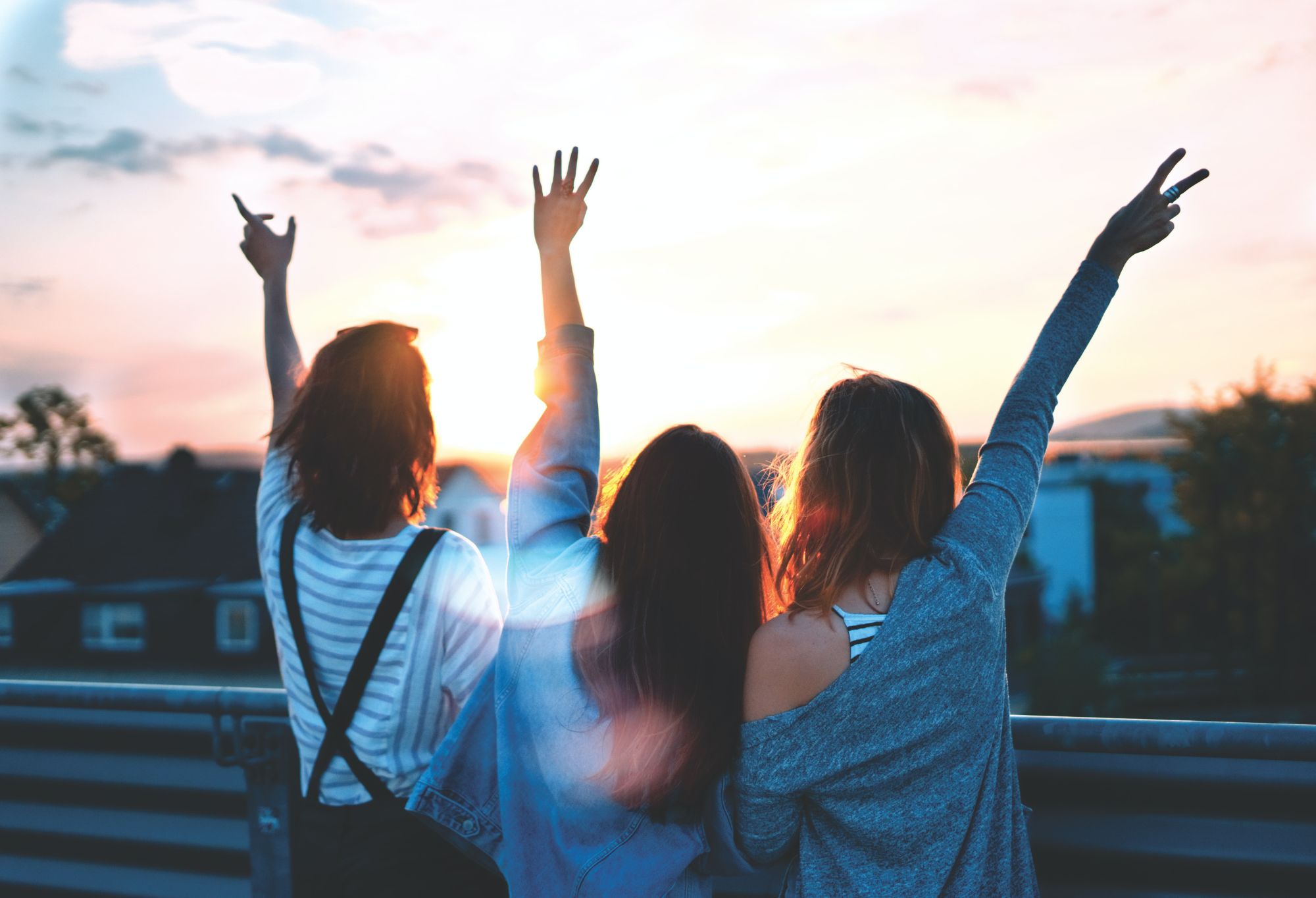 Three college students with long hair raise their arms to the sunset